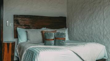 Un dormitorio con cabecera de madera, cama con colcha a rayas blancas y verdes, y pared de piedra.