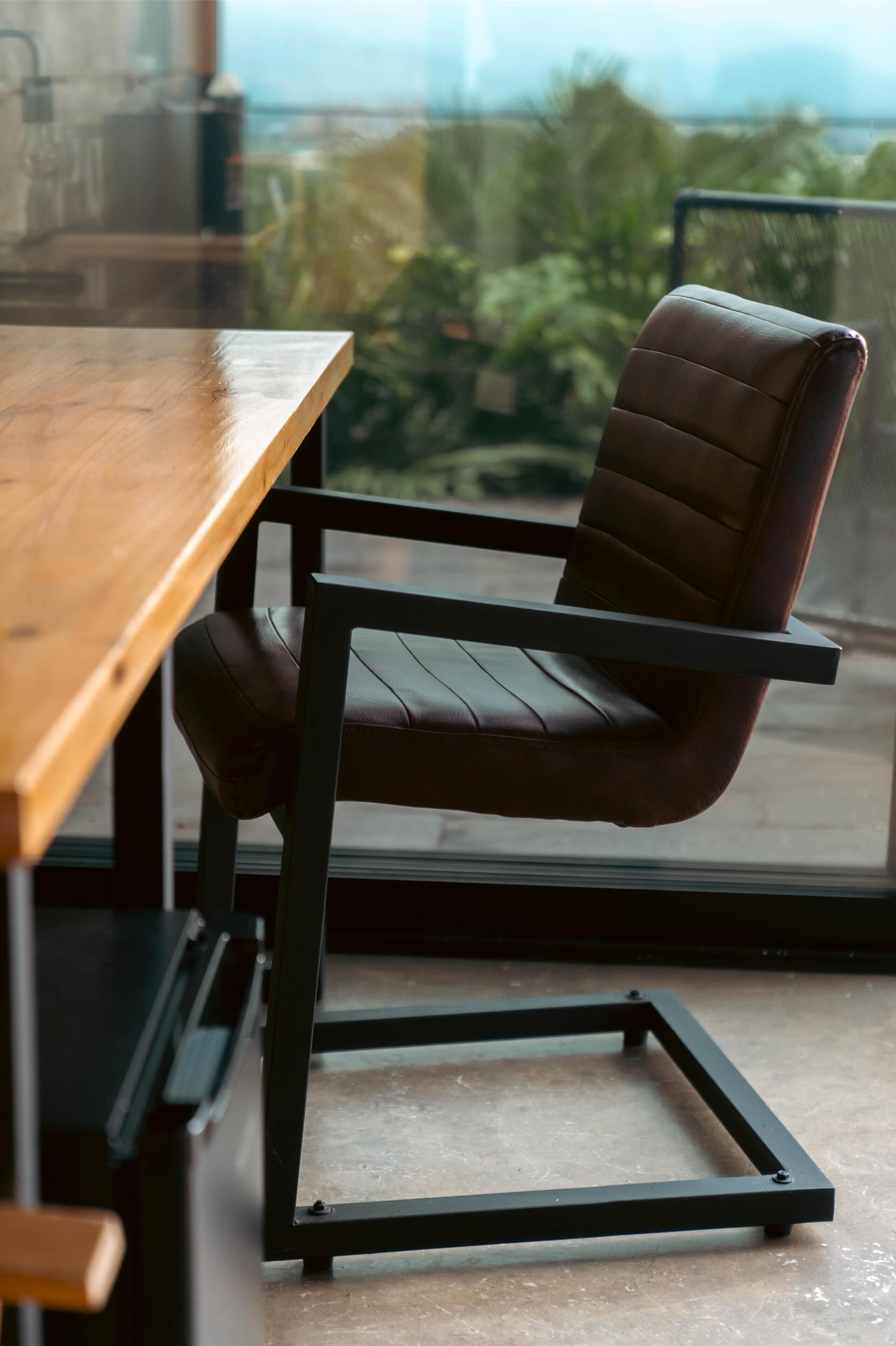 Une chaise moderne dotée d’un haut dossier et une table en bois, dans une pièce offrant une vue sur la verdure environnante.