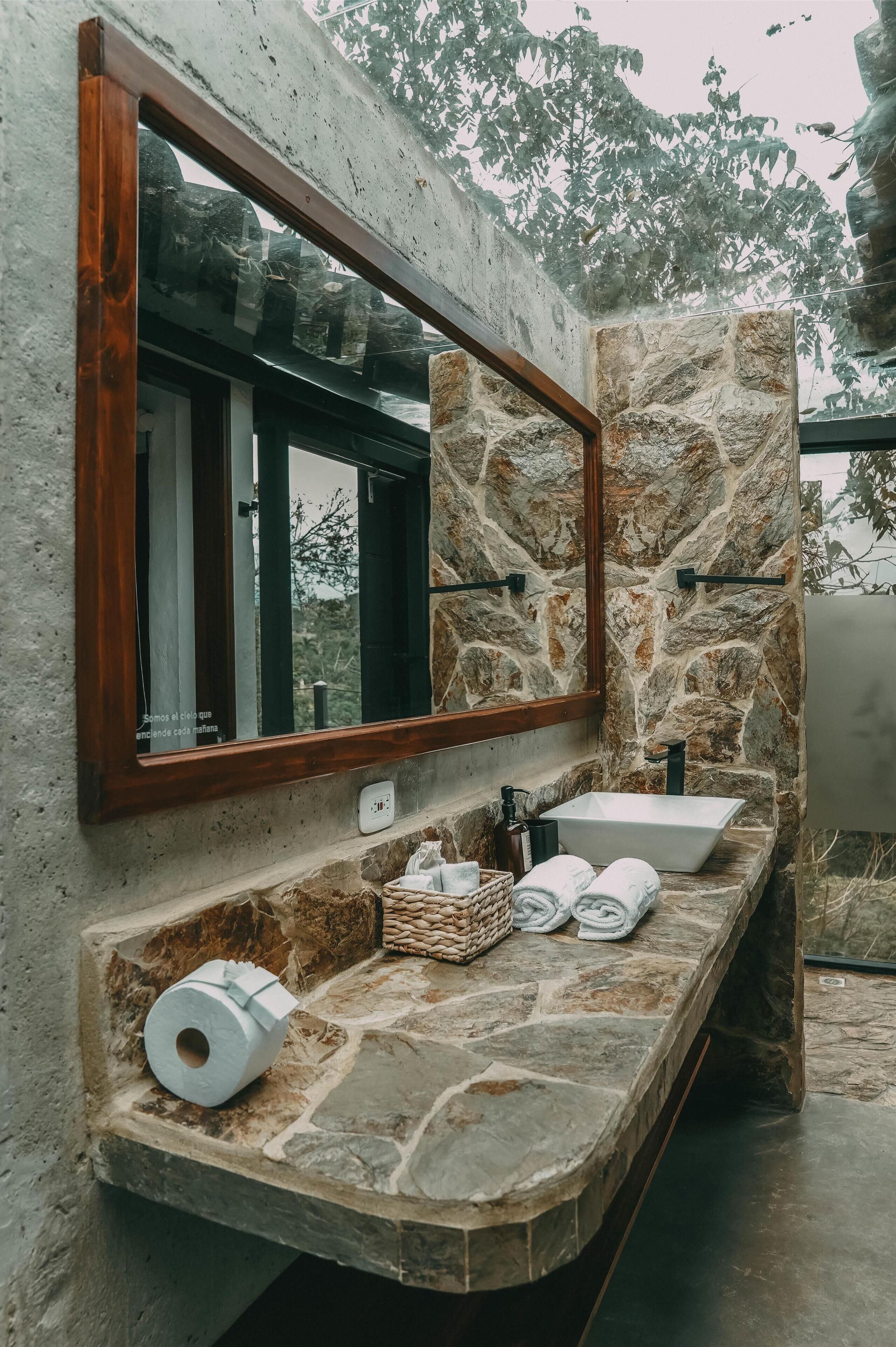 Une salle de bain avec un comptoir en pierre, un grand miroir, un lavabo et une fenêtre.