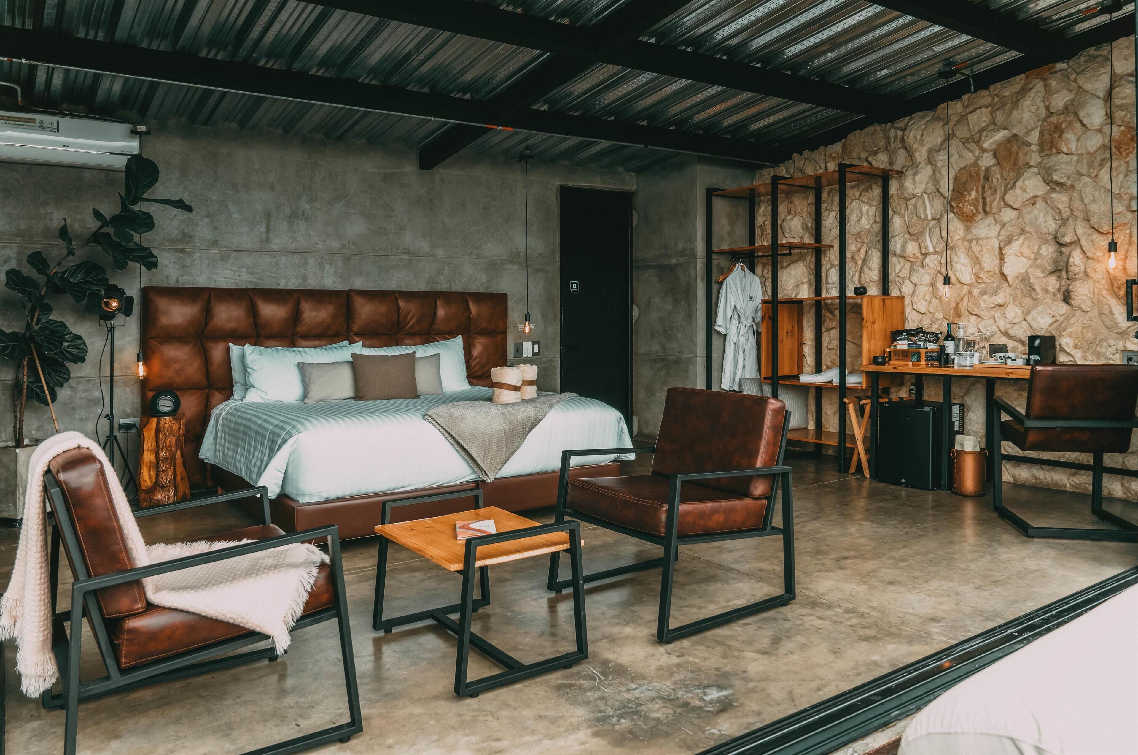 Une chambre moderne avec un grand lit, un coin salon avec une table basse et un mur en pierre.