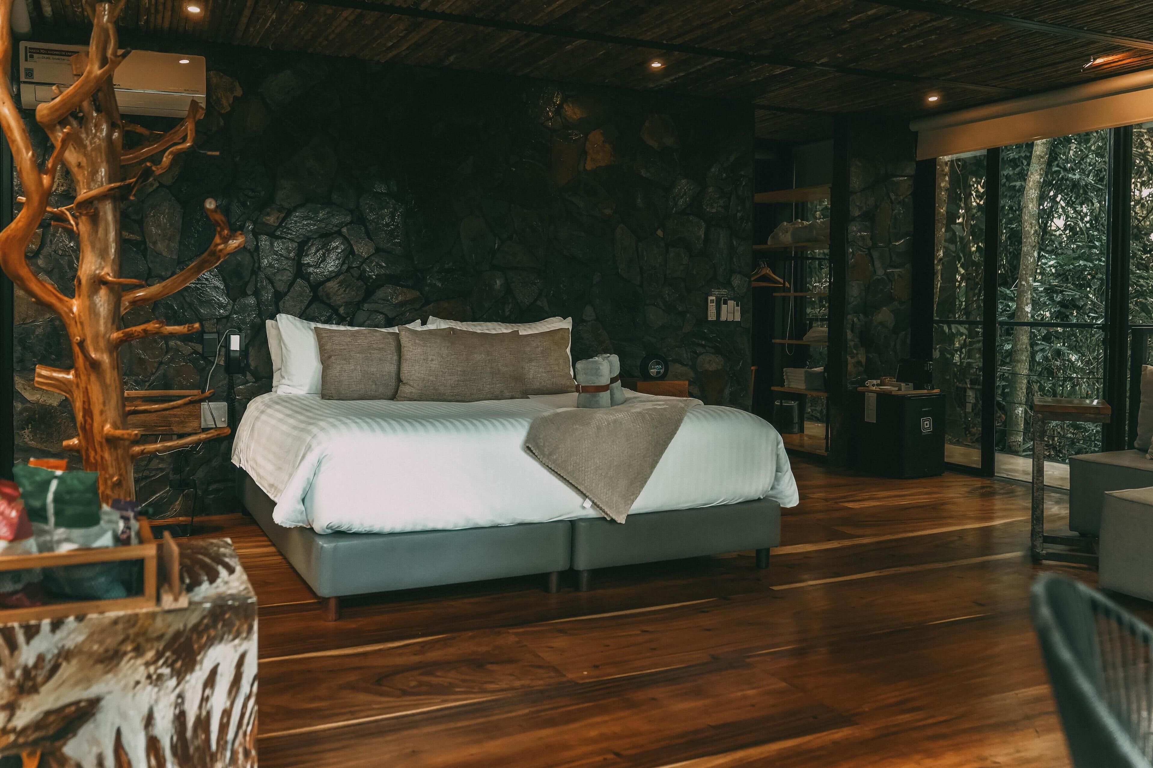 Un dormitorio moderno con pared de piedra, una cama grande y una escultura de árbol de madera.