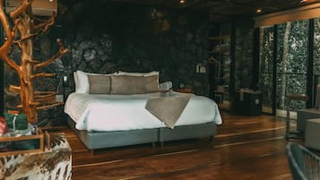 Un dormitorio moderno con pared de piedra, una cama grande y una escultura de árbol de madera.