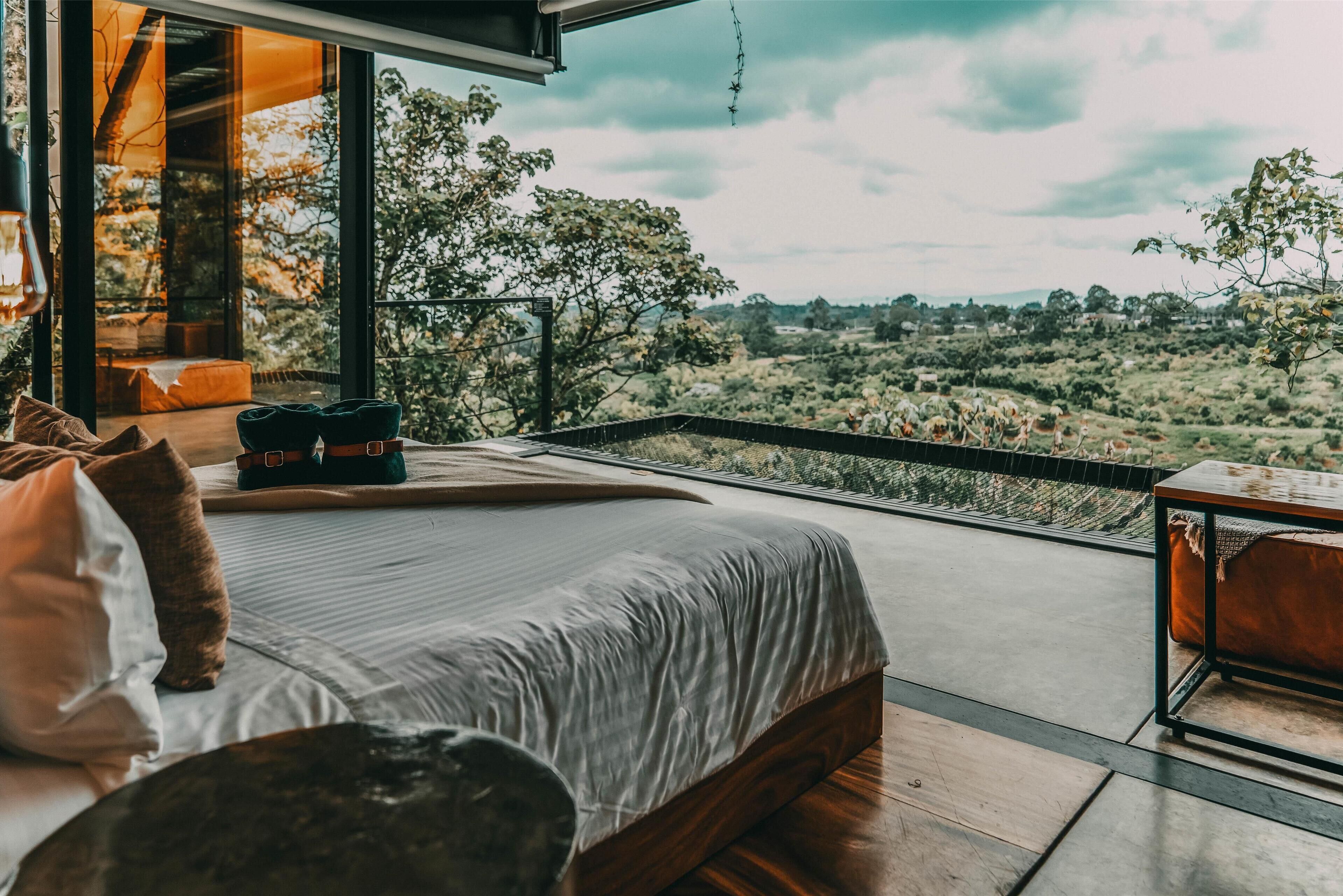 A bedroom with a large bed, a view of the countryside, and a balcony with a table and chairs.