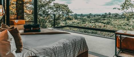 A bedroom with a large bed, a view of the countryside, and a balcony with a table and chairs.