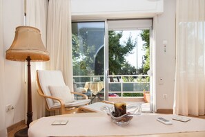 A hotel room with a large sliding glass door to a balcony, a wooden chair, a table with a lamp, and a bowl of fruit.