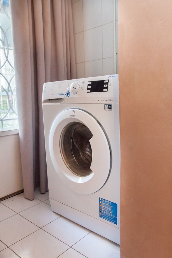 A front-loading washing machine in a bathroom with a window and curtains.