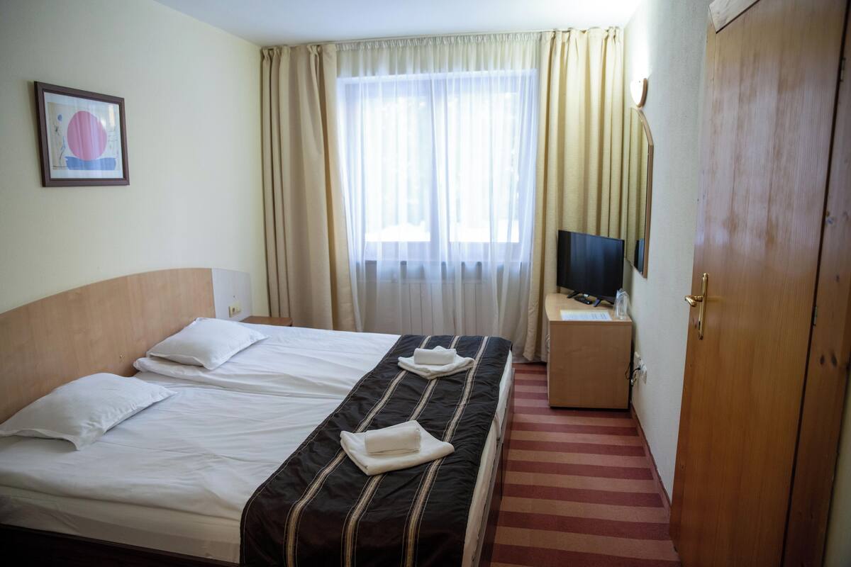 A hotel room with two beds, a television on a small table, and a door.