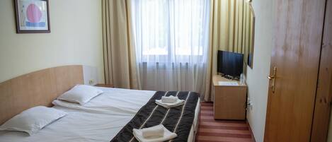 A hotel room with two beds, a television on a small table, and a door.