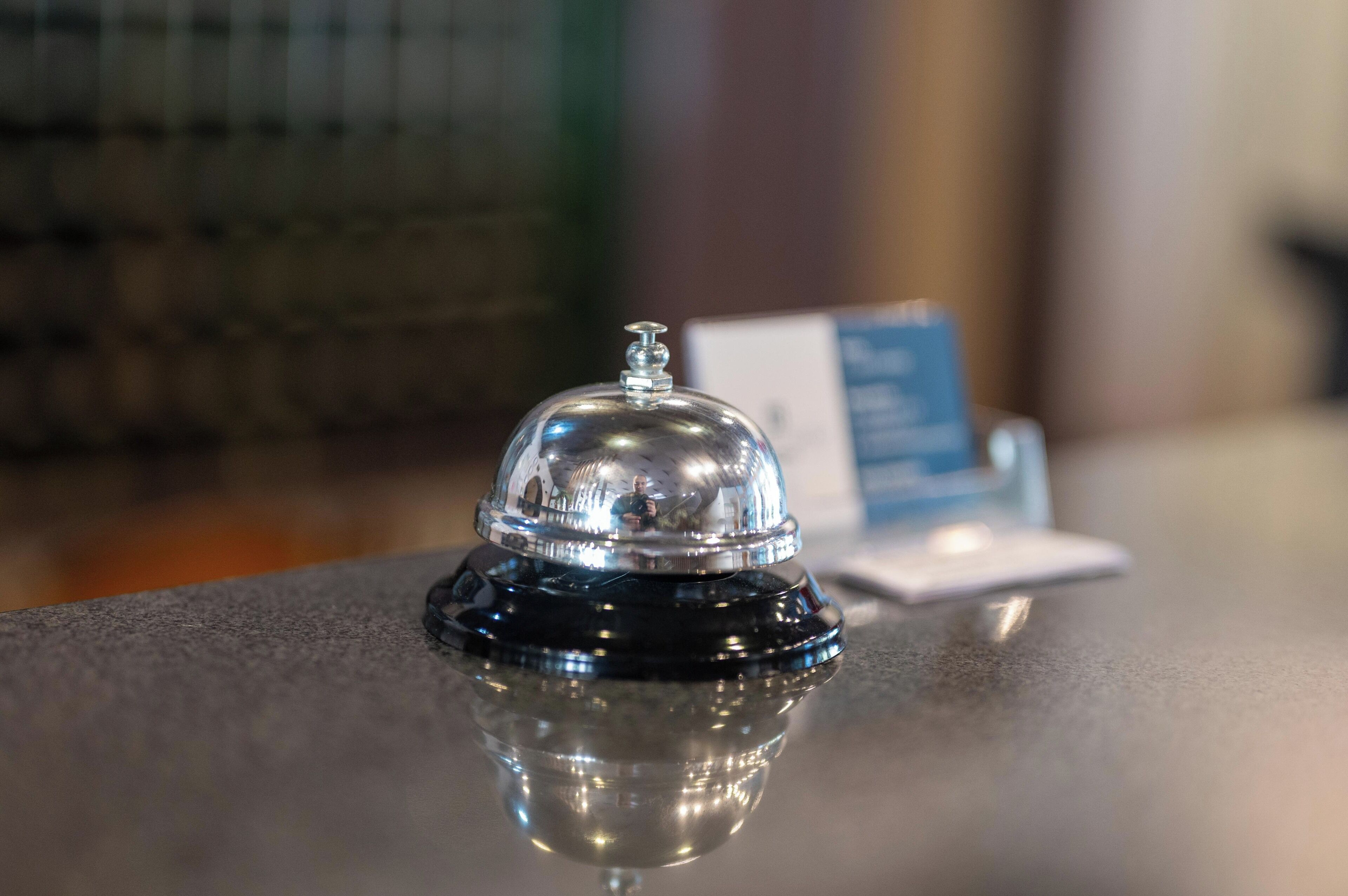 A hotel reception area with a reflective black counter, a silver bell, and a blue sign with text.