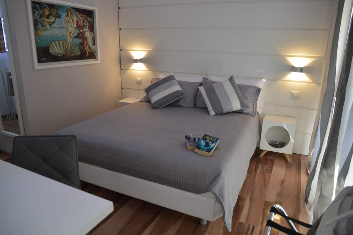 Cama bem arrumada com almofadas listradas, mesa de cabeceira com um livro e óculos, e um quadro na parede.