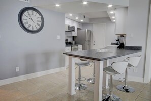 A modern kitchen with a central island, bar stools, and a wall-mounted clock.