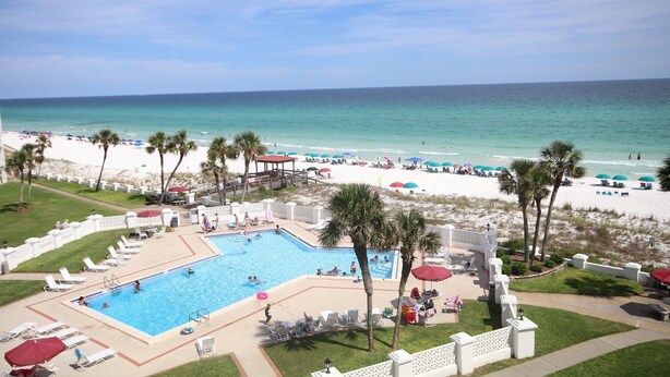 A resort with a swimming pool, beach, and palm trees.