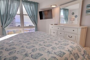 A bedroom with a bed, a dresser, a TV, and a window with curtains.