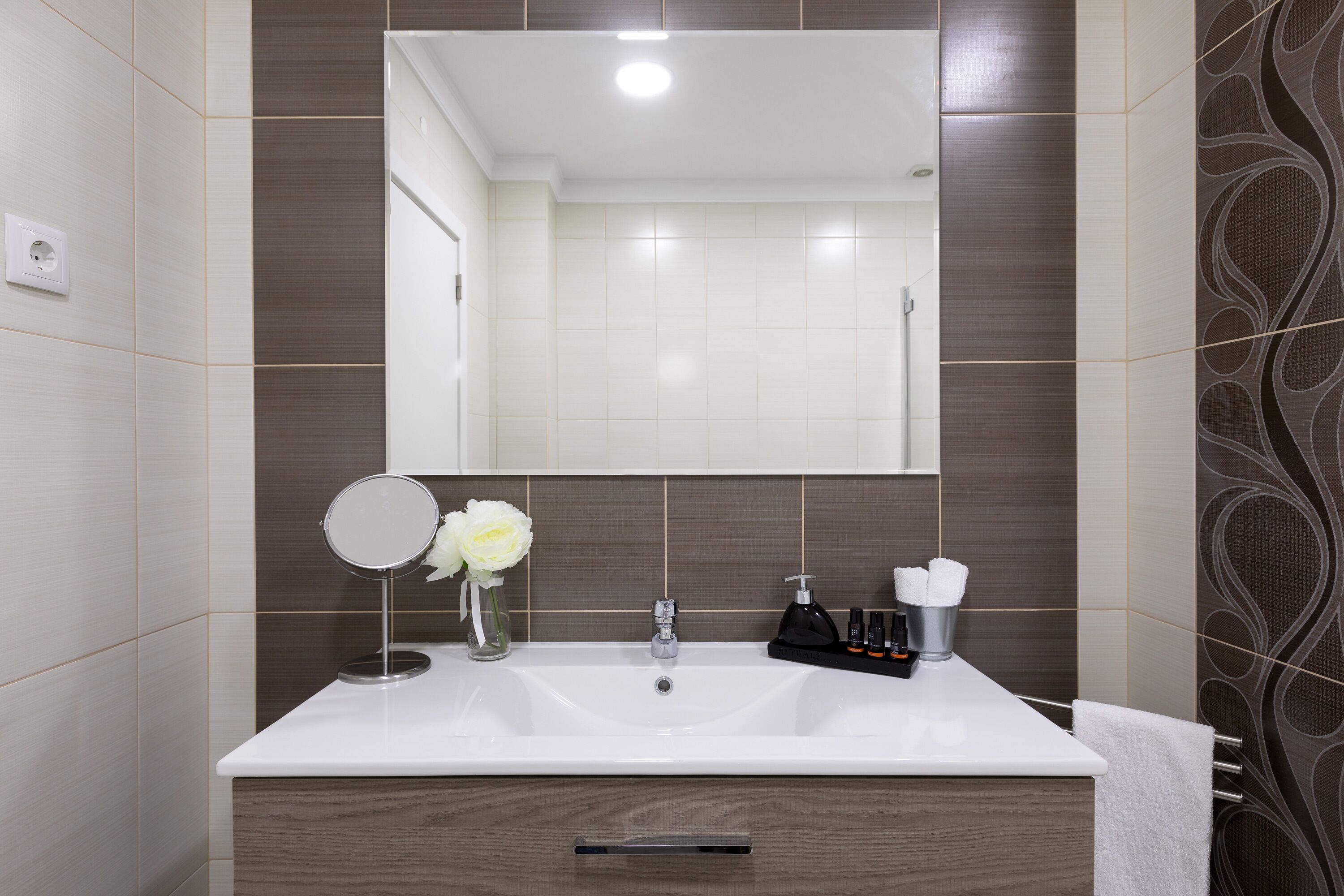 Een moderne badkamer met een grote spiegel, een witte wastafel en een meubel met een handdoekhouder.