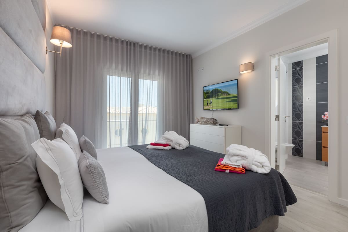A modern hotel room with a large bed, a flat-screen TV mounted on the wall, and a view of a golf course through the window.