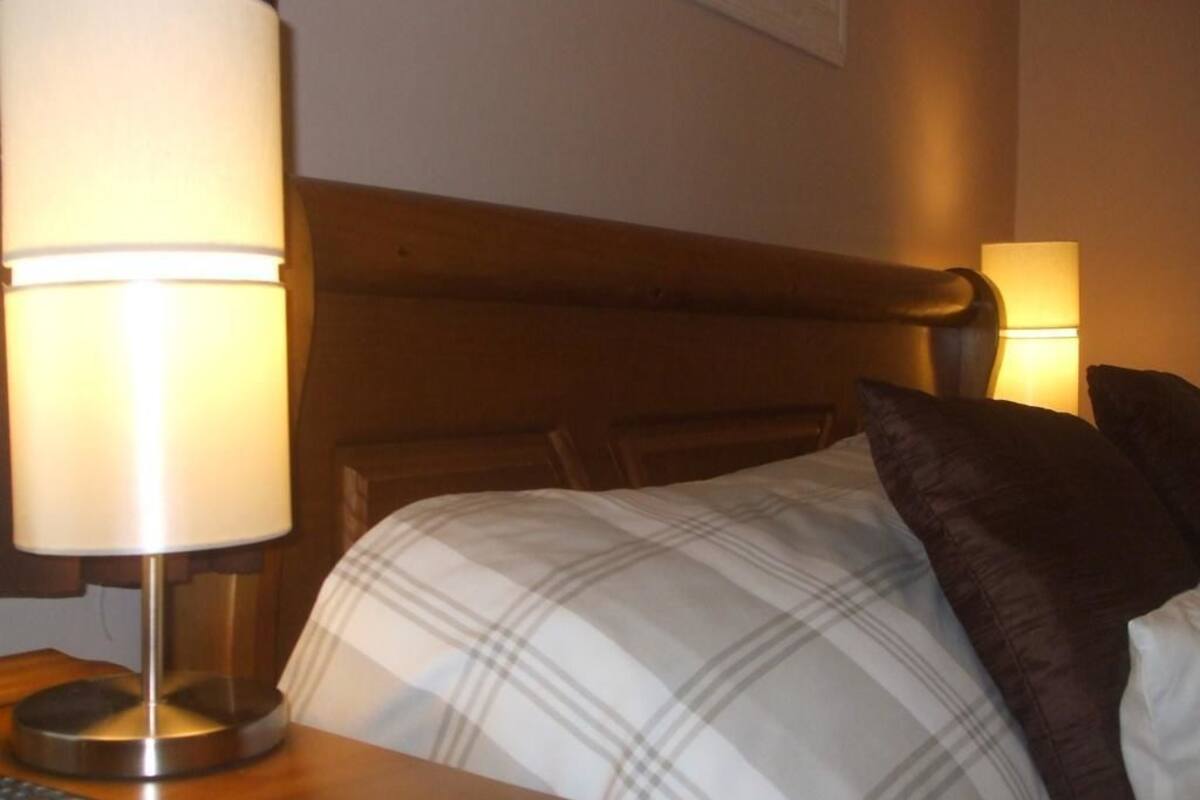 A hotel room with a bed, a nightstand, a lamp, and a remote control.