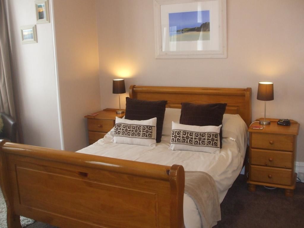 A wooden bed with two pillows, a nightstand with a lamp, and a framed picture on the wall.