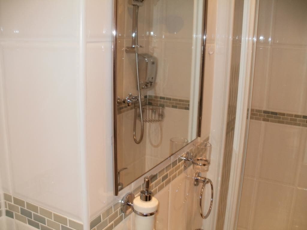 Ducha con cerramiento de vidrio, cabezal de ducha manual y grifo de mano.