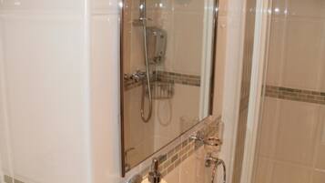 A glass-enclosed shower with a handheld showerhead and a handheld faucet.