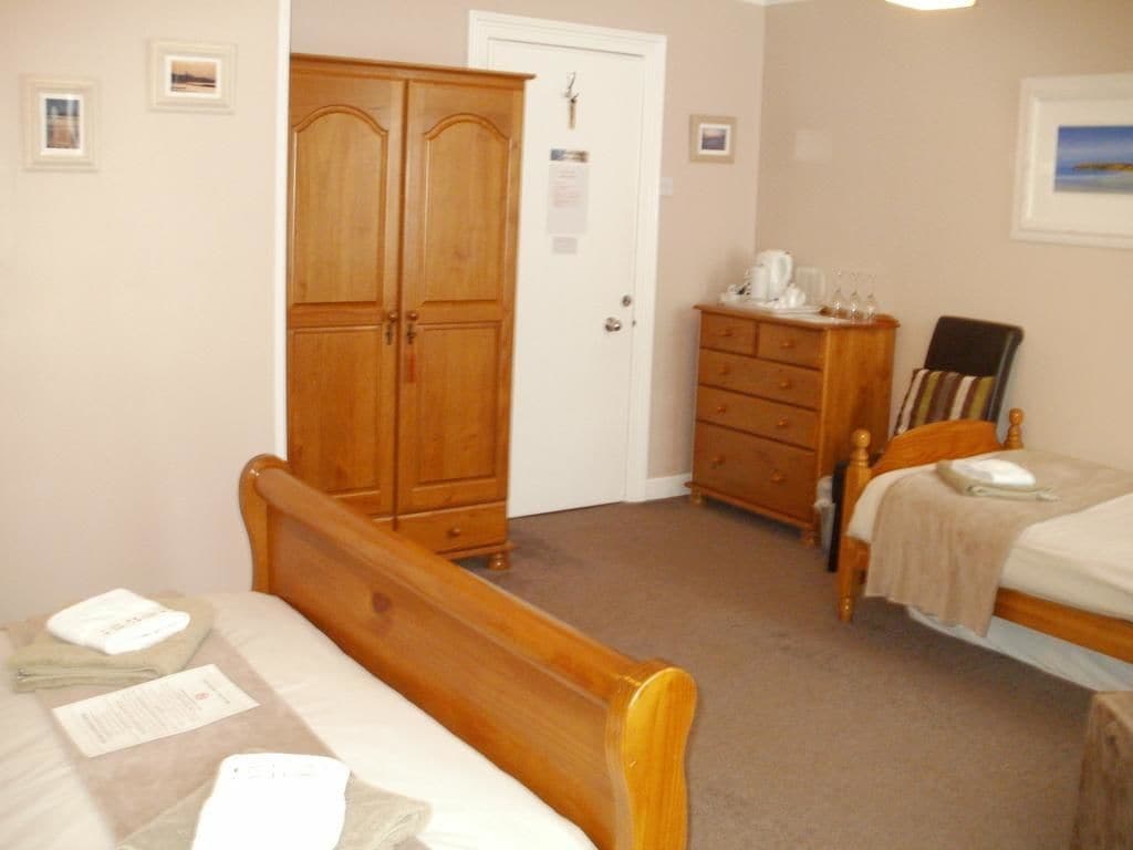 Een slaapkamer met een houten bed, een kledingkast van hout, een dressoir en een klein tafeltje met een stoel.