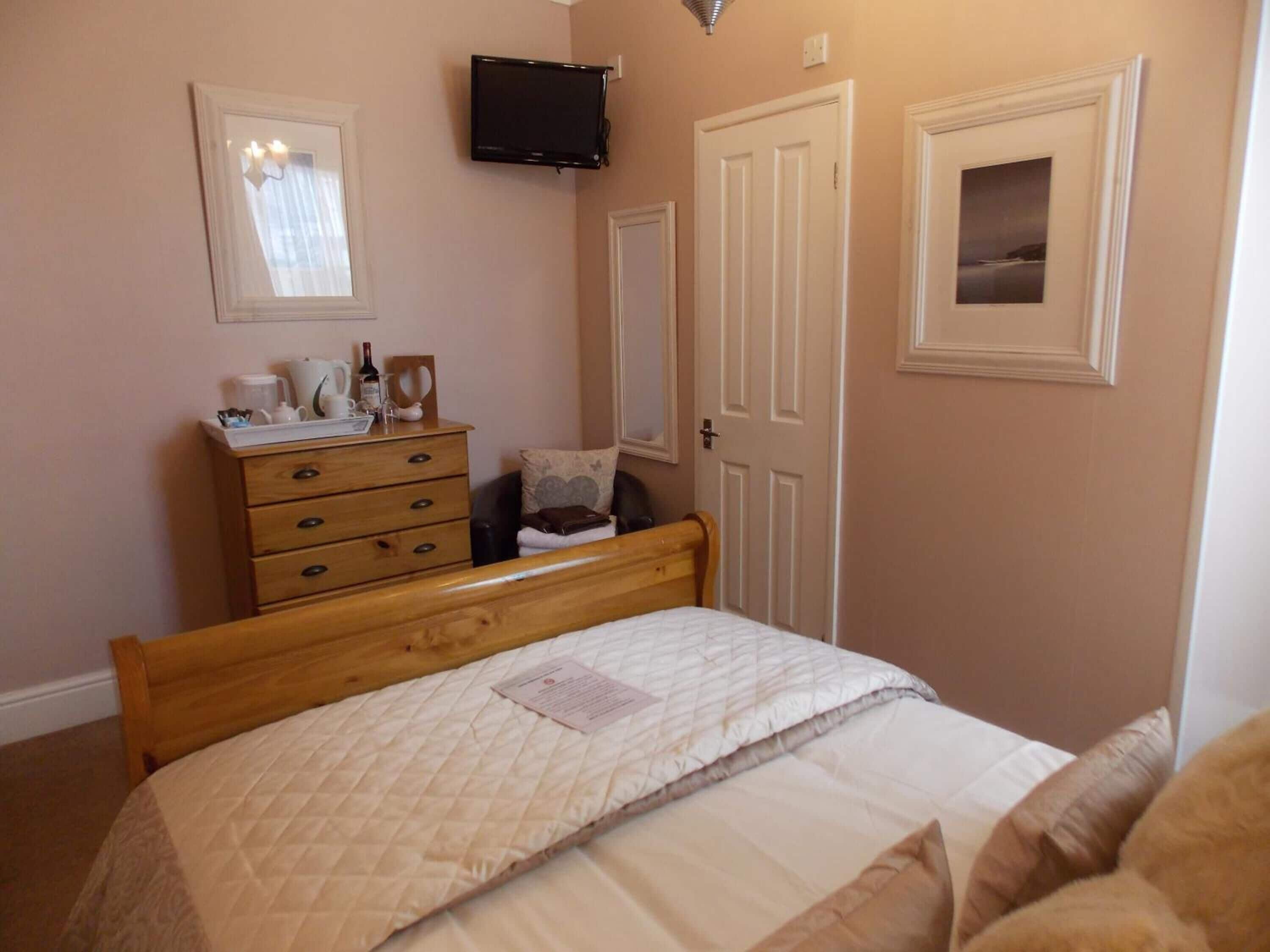 A bedroom with a bed, a dresser, a television mounted on the wall, and a door.
