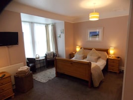 Habitación de hotel con cama de madera, lámparas de noche, escritorio, silla, televisión y ventana con cortinas.