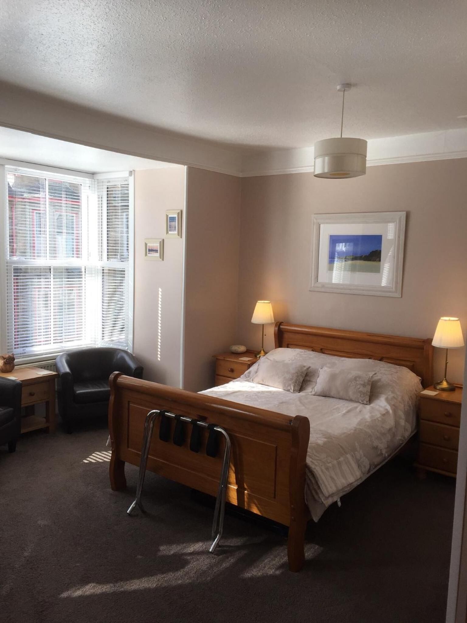 Une chambre à coucher bien rangée, avec un lit en bois, des lampes de chevet, une chaise et une fenêtre avec des stores.