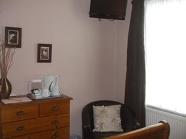 Una habitación con un aparador de madera, un sillón negro con cojín floral, una estación de café y dos cuadros en la pared.