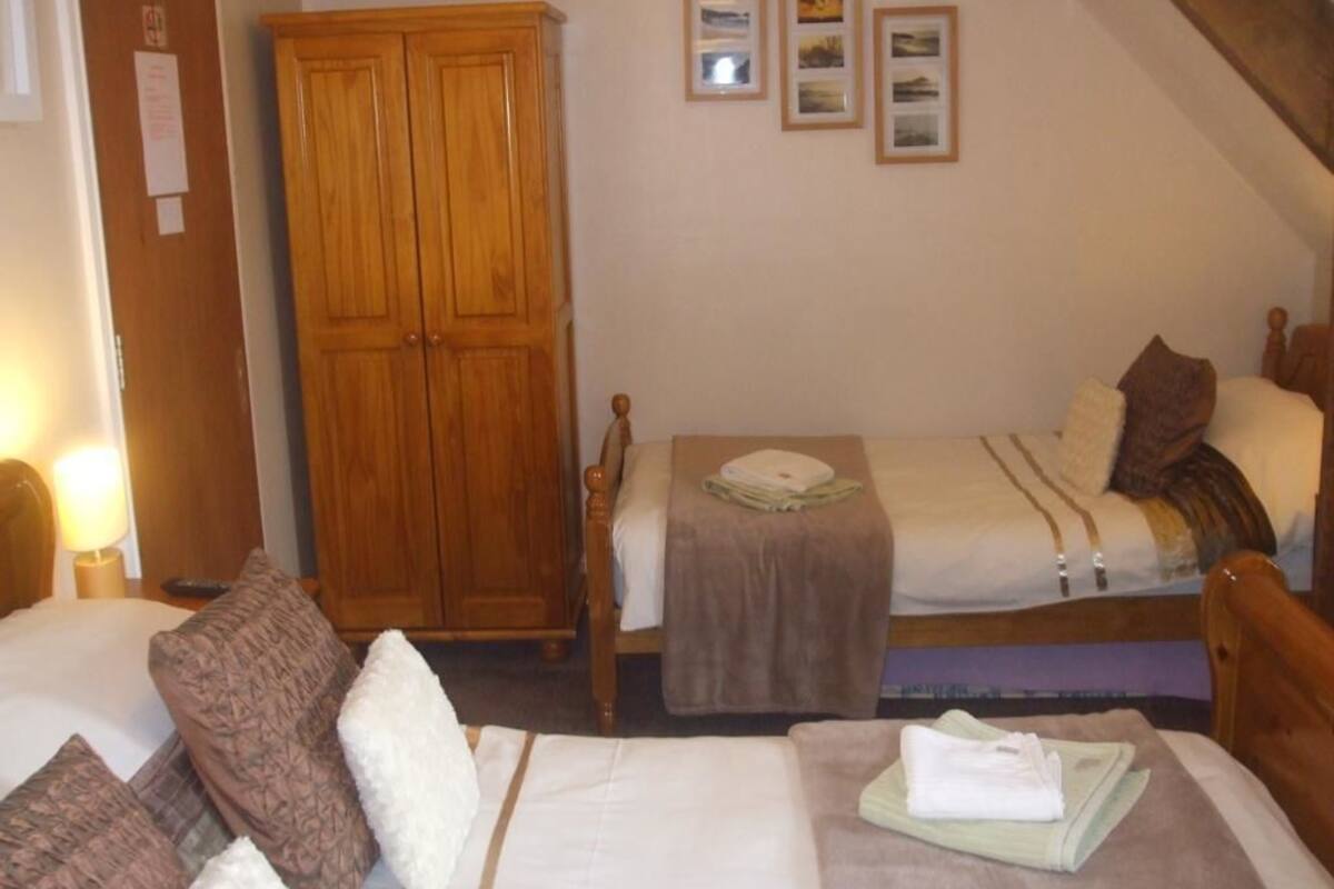 A bedroom with two beds, a wardrobe, and a bedside table.