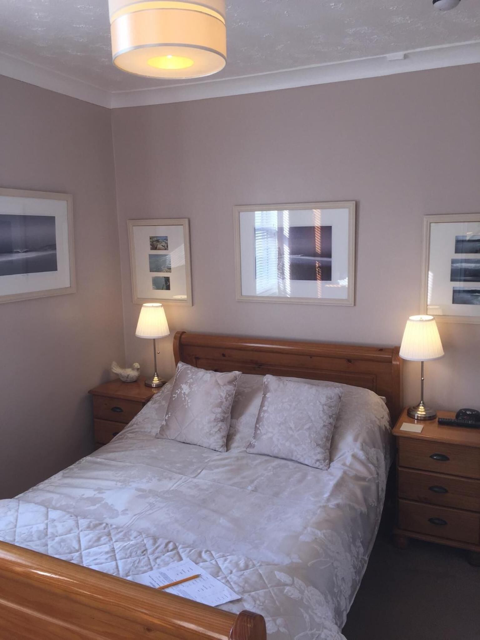 A neatly made bed with a quilted cover, two bedside tables with lamps, and framed pictures on the walls.