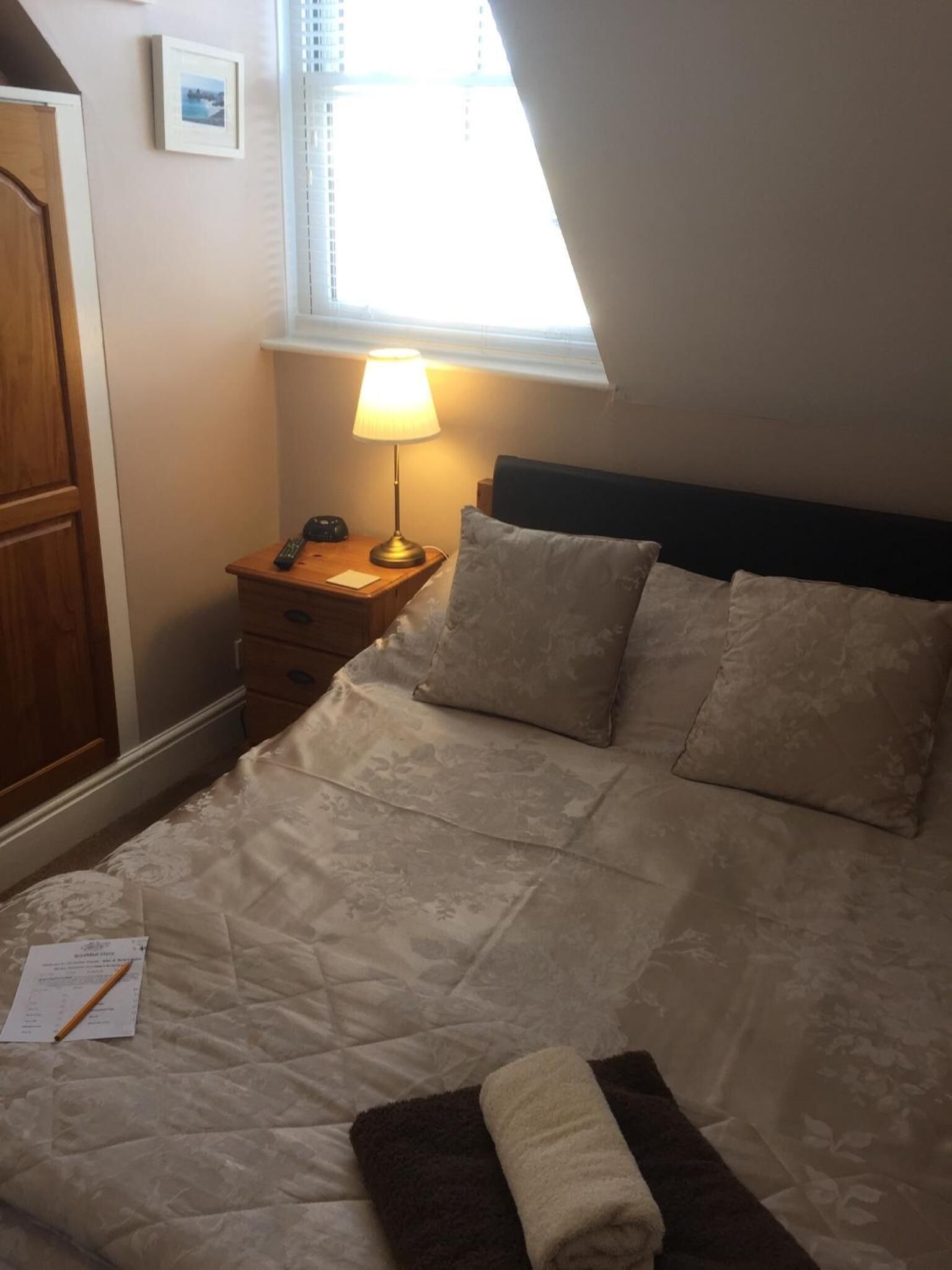 Een slaapkamer met een bed, nachtkastje, lamp, raam en deur.