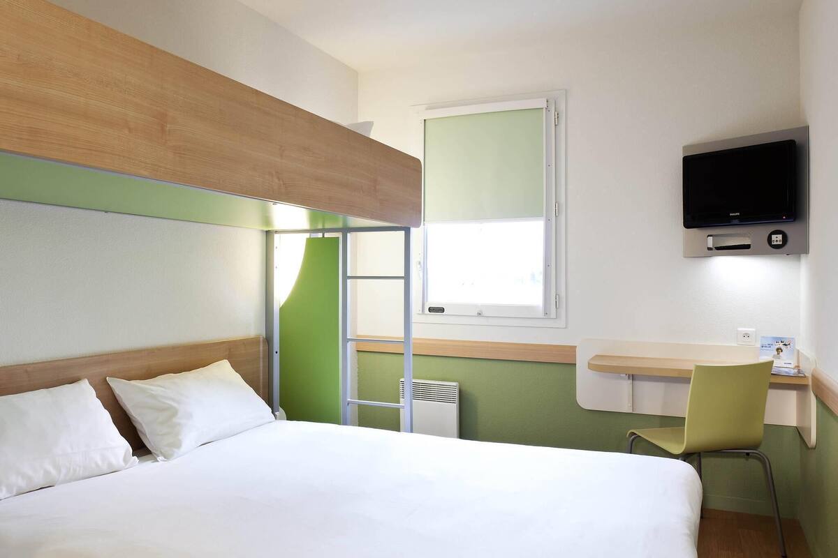 Ein Hotelzimmer mit Bett, Schreibtisch mit Stuhl, einem an der Wand befestigten Fernseher und einem Fenster.