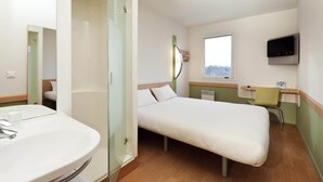 A hotel room with a bed, a bedside table, a TV, a window, and a bathroom with a sink and mirror. - ibis budget Mantes-la-Jolie Sully (Mantes-la-Jolie)