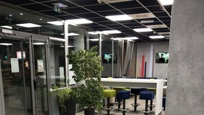 An office space with glass partitions, a large potted plant, and a white table with colorful stools. - ibis budget Mantes-la-Jolie Sully (Mantes-la-Jolie)