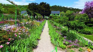 A garden pathway with various plants and flowers, surrounded by greenhouses and trees. - ibis budget Mantes-la-Jolie Sully (Mantes-la-Jolie)