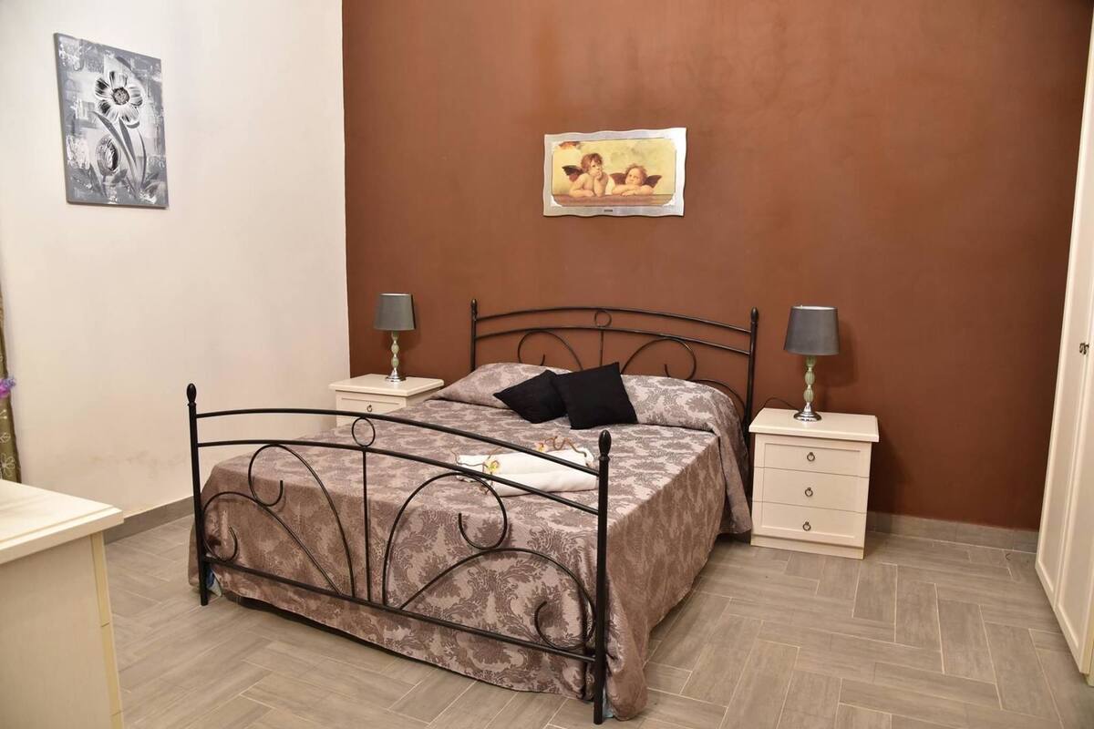 Ein Schlafzimmer mit einem Bett, zwei Nachttischen mit Lampen, einem Beistelltisch, einer Wand mit einem Gemälde und einem Sessel.