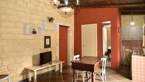 Une pièce avec un mur en briques, une table en bois, un téléviseur et un coin cuisine équipé de placards et d’un évier.