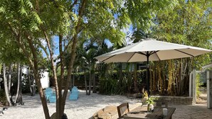 Un espace patio aménagé avec une table et des chaises en bois, un grand parasol et un mur en pierre.