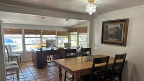 Un coin repas avec une table et des chaises en bois, un ordinateur posé sur un bureau et un tableau accroché au mur.