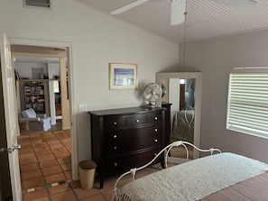 A bedroom with a bed, a dresser, a fan, a mirror, and a window with blinds.