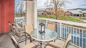 Ein Balkon mit rundem Glastisch und Stühlen, mit Blick auf einen Fluss und Gebäude im Hintergrund.
