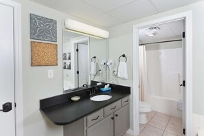 A bathroom with a sink, mirror, towel rack, and shower area. - Bear Crossing 301 (Pigeon Forge)