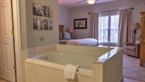 A bathroom with a large bathtub, a ceiling fan, and a window with curtains.