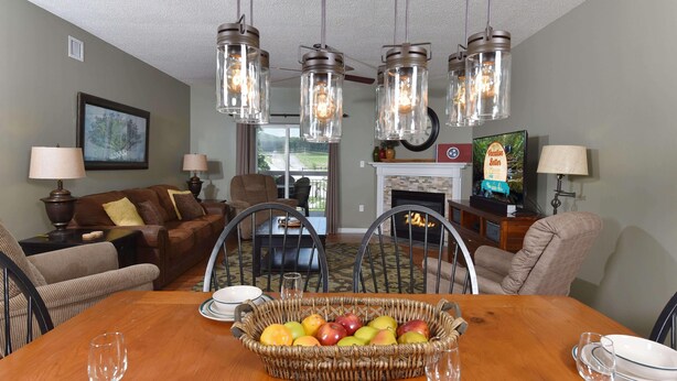 A dining area with a wooden table, wicker basket with fruits, and hanging light fixtures.