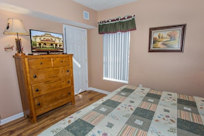 A bedroom with a wooden dresser, a television, a window with blinds, and a quilt on the floor. - Bear Crossing 202 (Pigeon Forge)