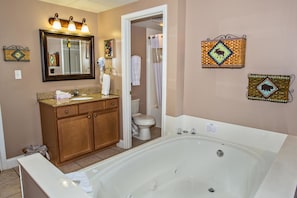 A bathroom with a large bathtub, wooden vanity, and a mirror with lights. - Bear Crossing 202 (Pigeon Forge)