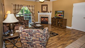 A living room with a fireplace, a television, and a ceiling fan. - Bear Crossing 202 (Pigeon Forge)