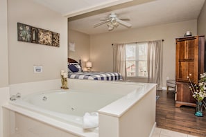 Une chambre spacieuse avec une grande baignoire blanche, une armoire en bois et un lit recouvert d’une courtepointe à rayures bleues et blanches.