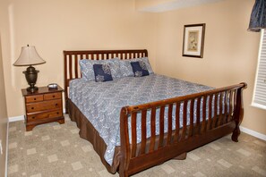Un dormitorio con una cama de madera, una mesita de noche con una lámpara y un cuadro enmarcado en la pared.