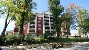 Un edificio de varios pisos con balcones, un arroyo en primer plano y follaje circundante.